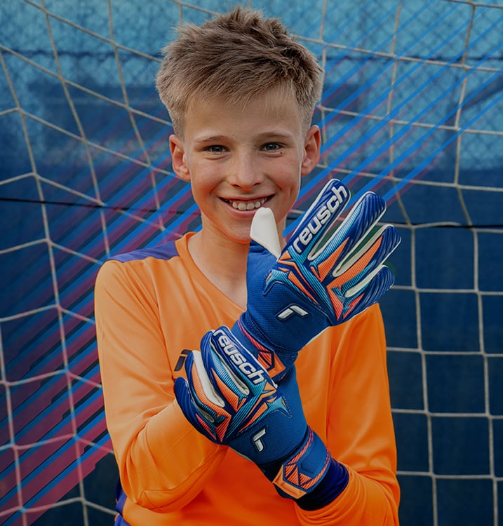 Junger Torwart mit blauen Reusch-Torwarthandschuhen vor dem Fußballtor