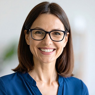 Porträt einer lächelnden Frau mit braunen Haaren und Brille, die eine dunkelblaue Bluse trägt.