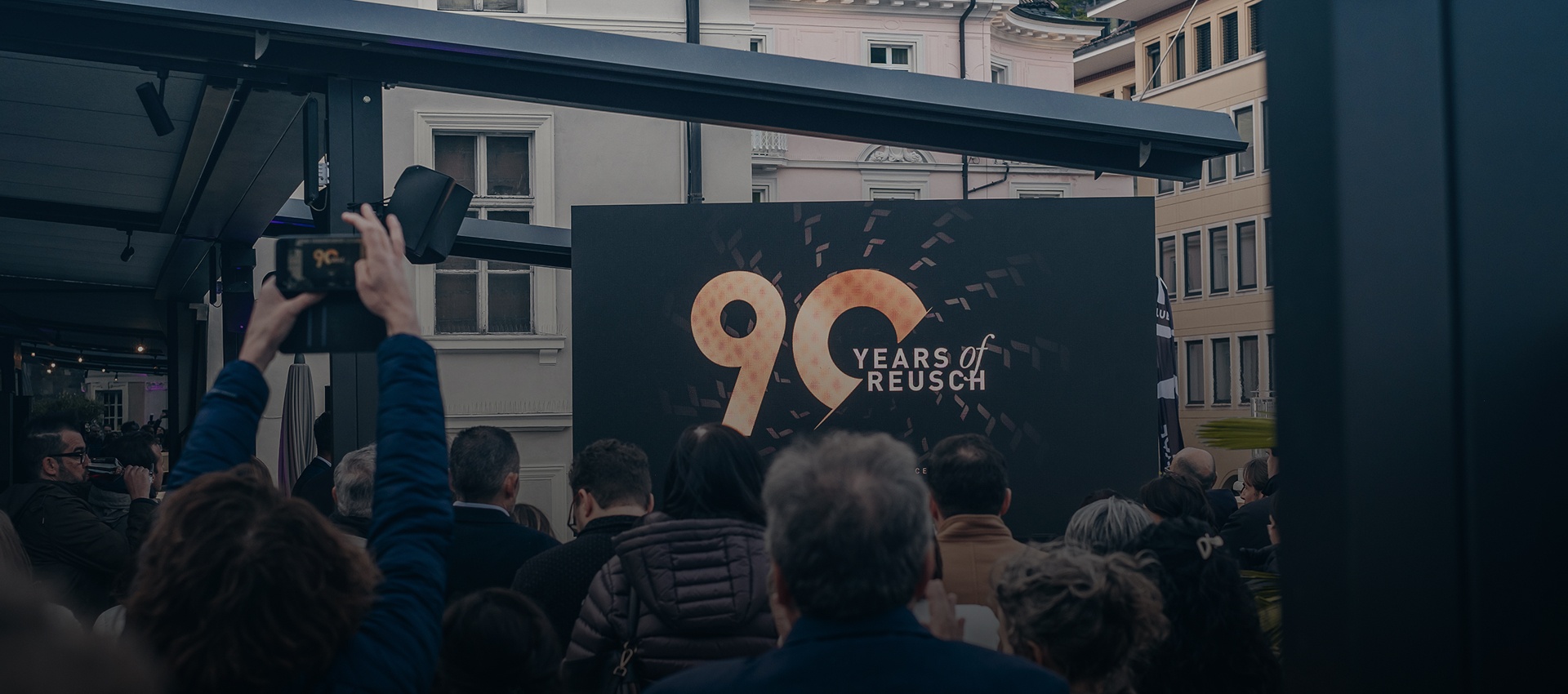 Crowd at an event celebrating Reusch\'s 90th anniversary, with a large screen in the background displaying the \'90 Years of Reusch\' logo.