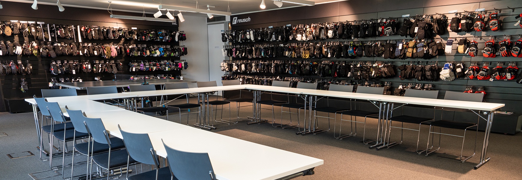 Moderner Meetingraum bei Reusch mit U-förmig angeordneten Tischen und Wänden voller ausgestellter Sport- und Wintersporthandschuhe.